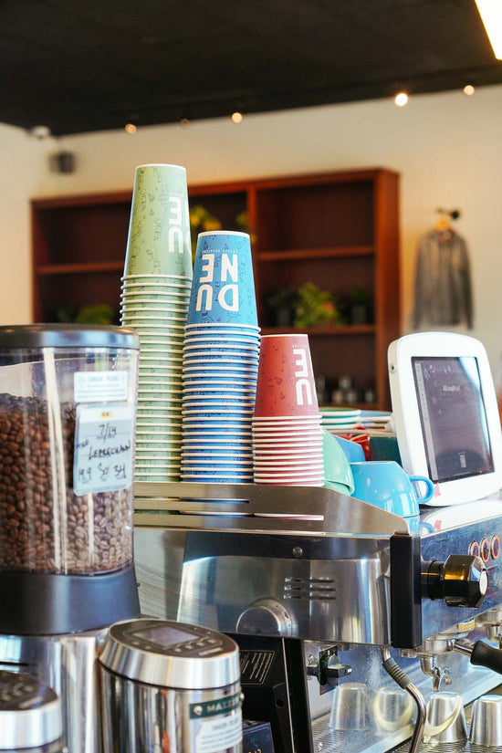 Dune coffee cups stacked on top of espresso machine at Storke location 